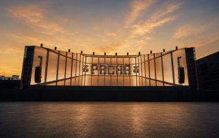 Outdoor concert stage at sunset with a backlit frame and large illuminated letters in the center, no people present.