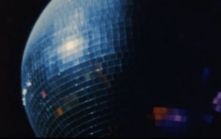 Close-up of a blue disco ball with mirrored tiles reflecting light against a dark background.